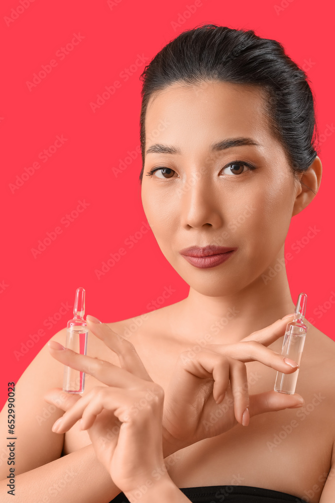 Beautiful Asian woman with ampules on red background. Skin care concept