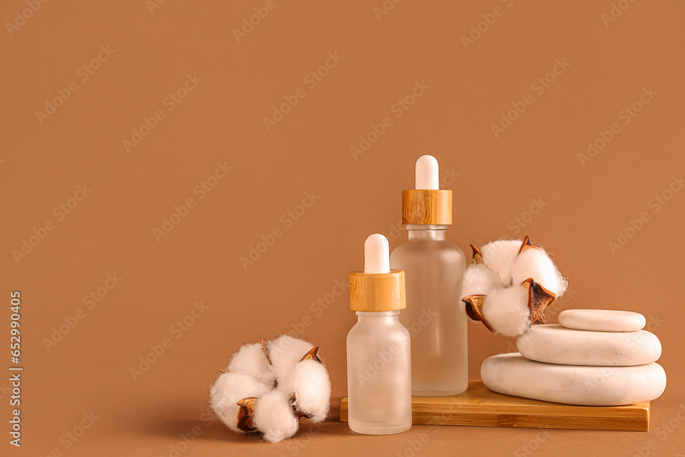 Bottles of essential oil, cotton flowers and spa stones on color background