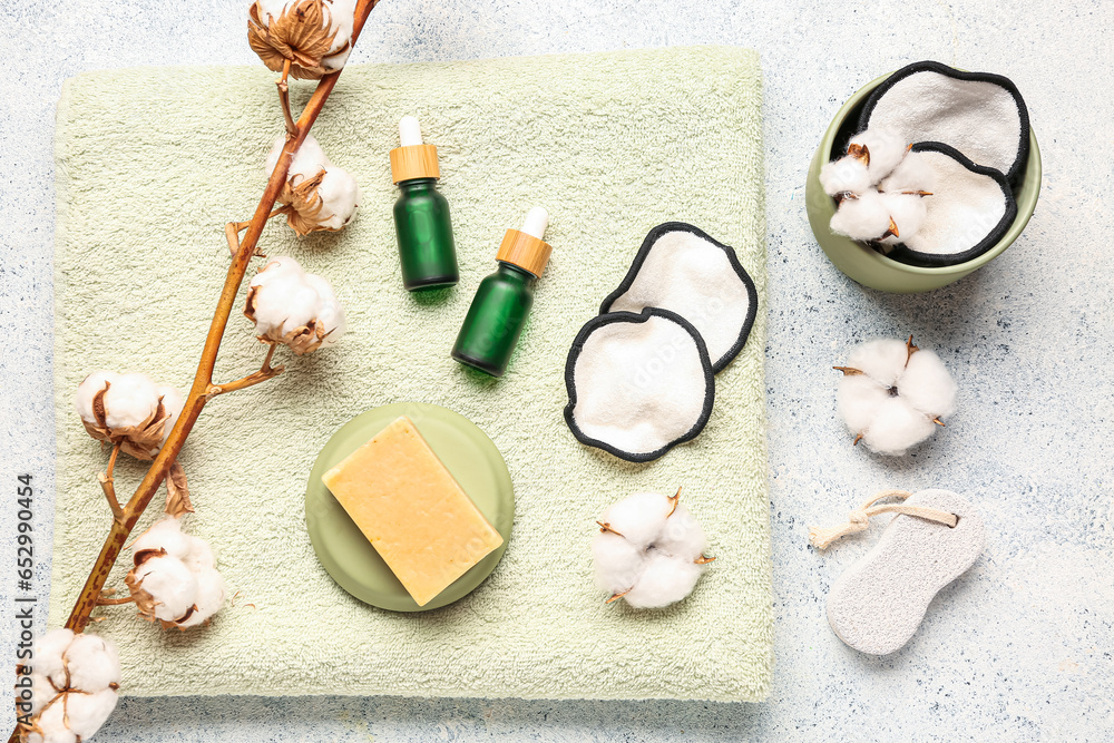 Bottles of essential oil, soap, clean towel, cotton flowers and pads on light background