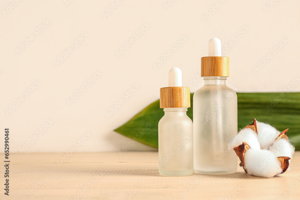 Bottles of essential oil and cotton flower on wooden background