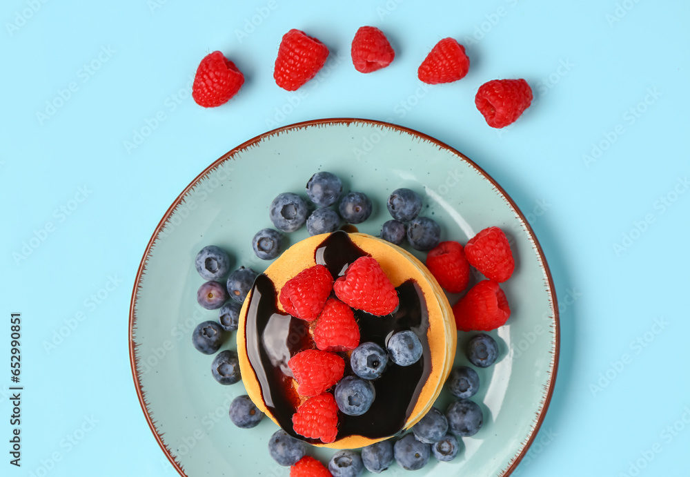 Plate with sweet pancakes and berries on blue background