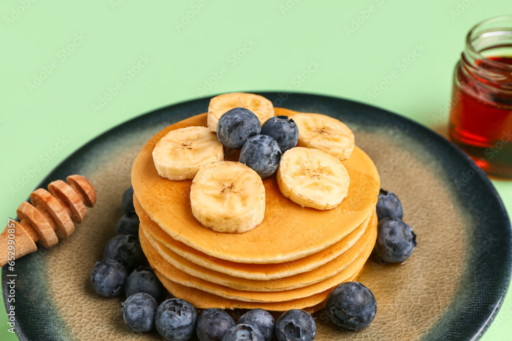 Plate with sweet pancakes, banana and blueberry on green background, closeup