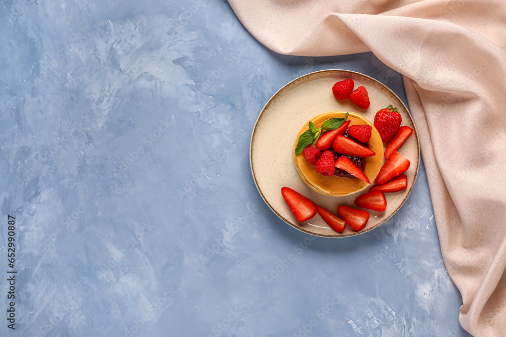 Plate with tasty pancakes and berries on blue background