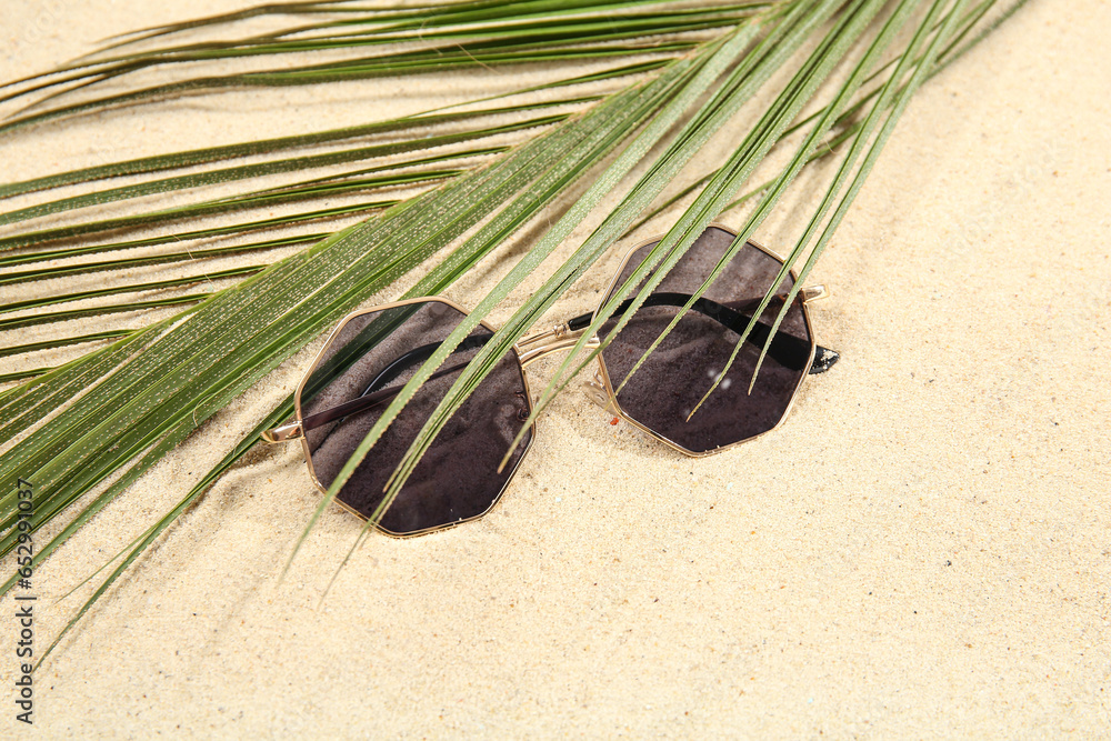 Palm leaf with stylish sunglasses on beige background