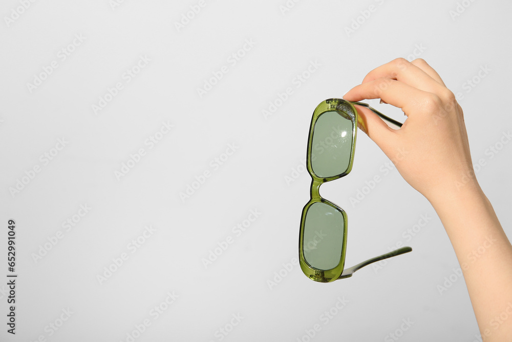 Female hand holding stylish sunglasses on white background