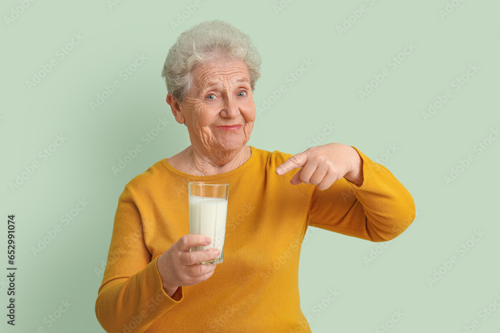 Senior woman pointing at glass of milk on green background