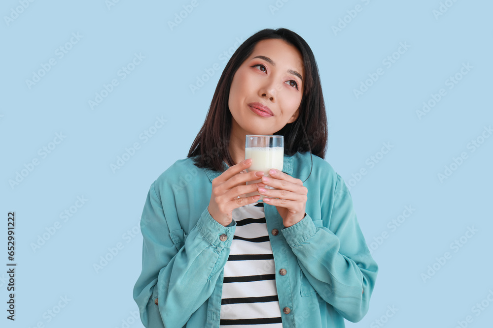 Beautiful Asian woman with glass of milk on light blue background