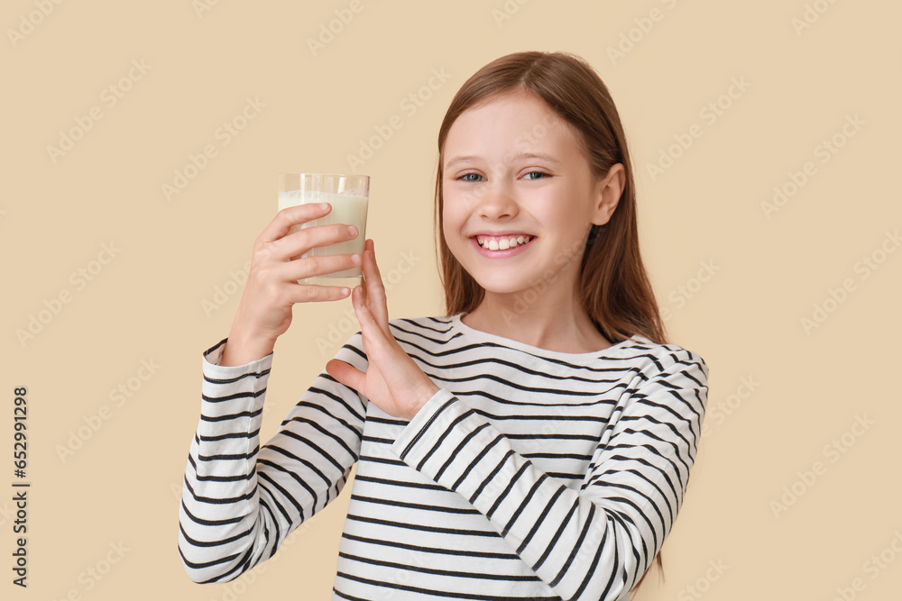 Little girl with glass of milk on beige background