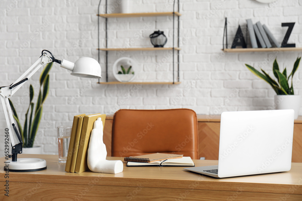 Workplace with laptop, stylish holder for books and lamp in room