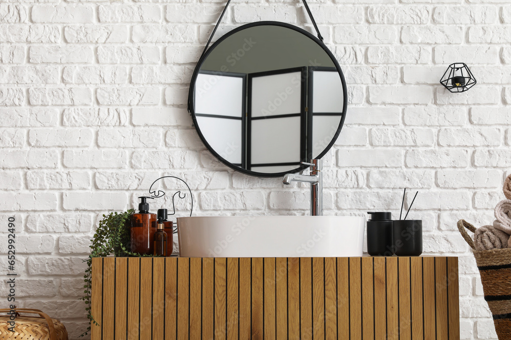 Sink bowl with bath accessories and mirror on wooden cabinet in bathroom