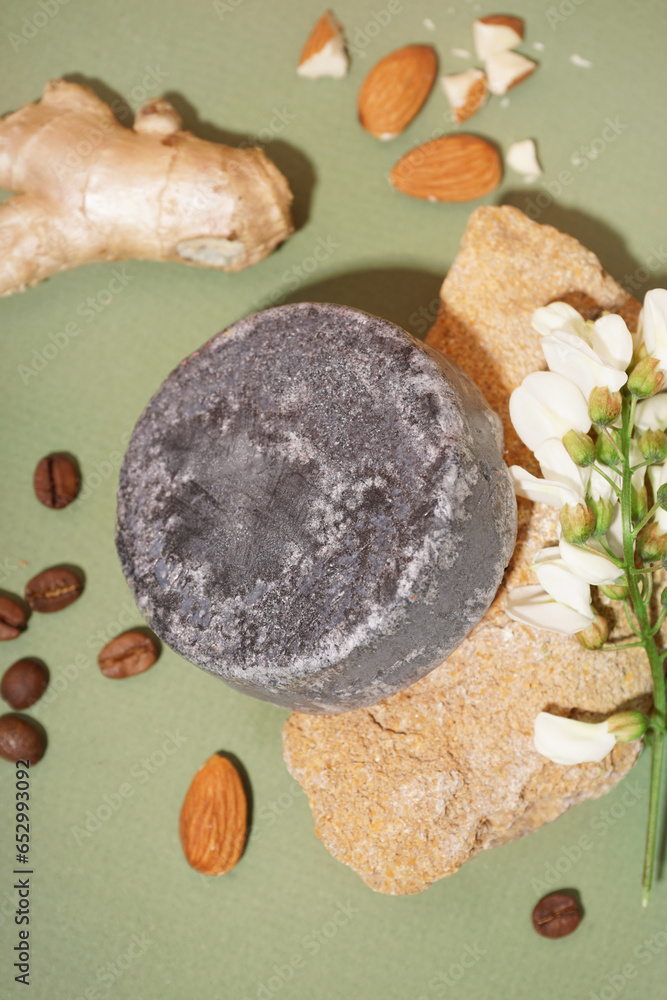 Grey solid shampoo bar with flower, ginger and coffee beans on green background