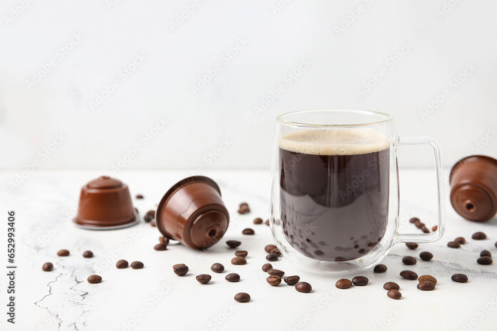 Cup of delicious coffee, pods and beans on white table