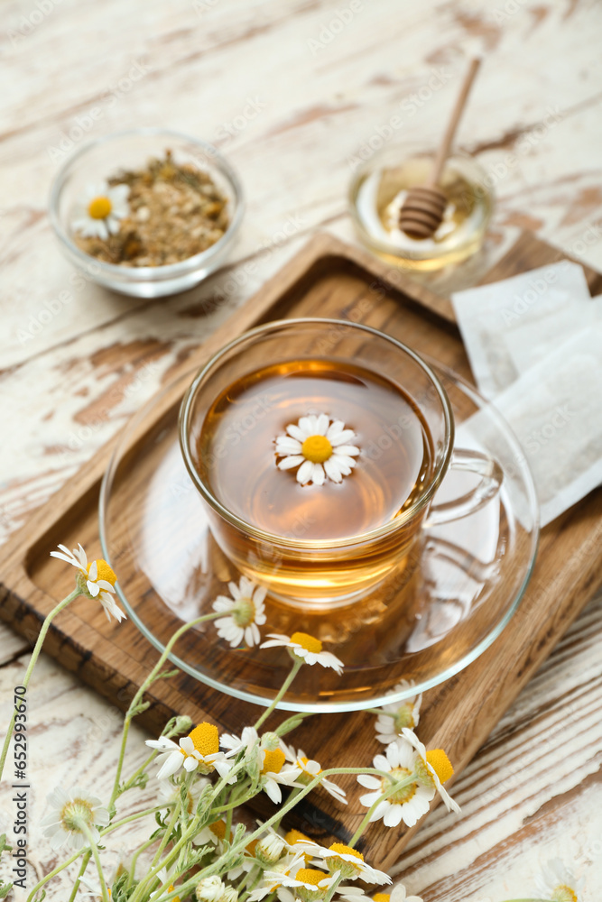 Cup of hot chamomile tea on light wooden background