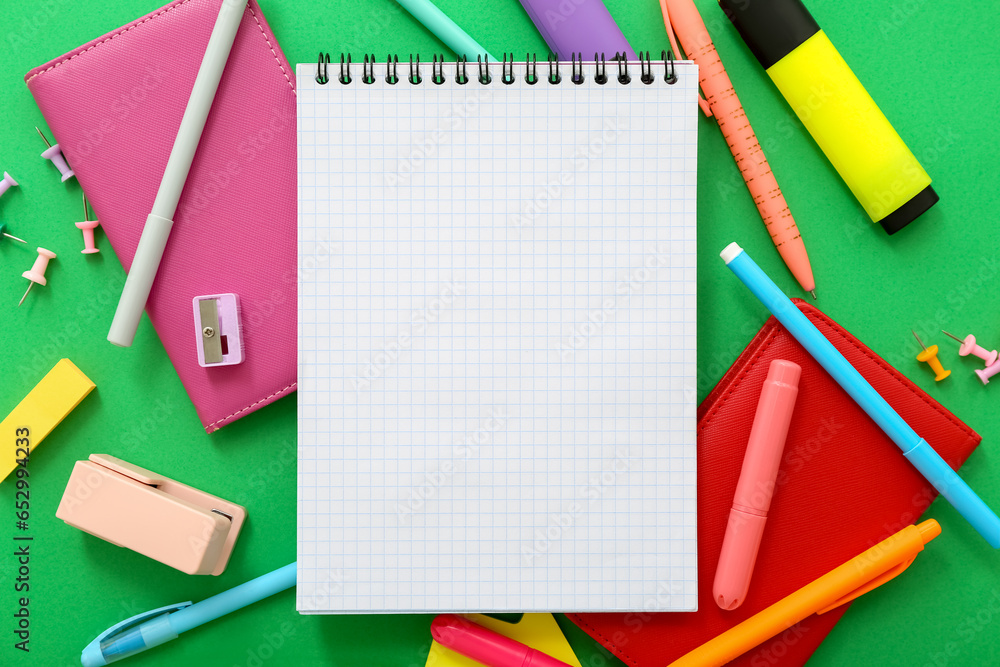 Composition with blank notebook and different stationery on green background