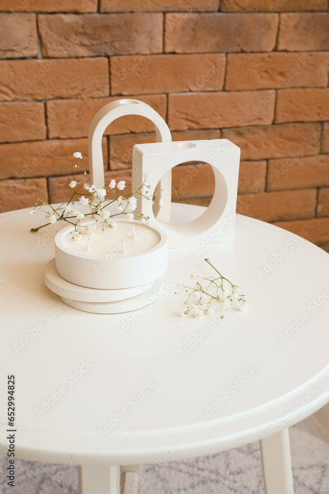 Gypsophila flowers and candle on table near brick wall in room, closeup