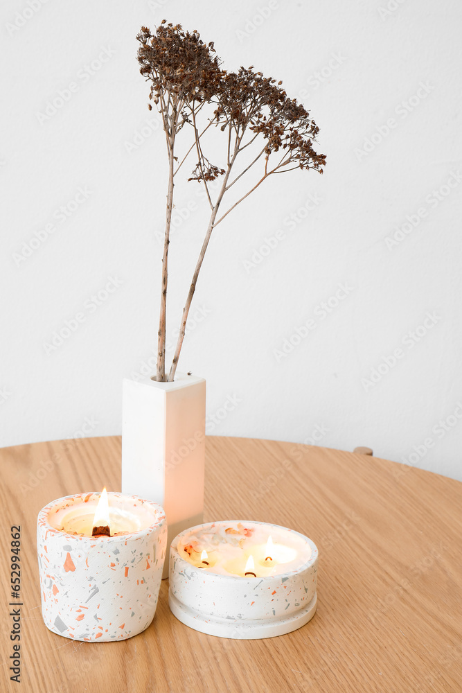 Burning candles and flowers on table near light wall in room, closeup