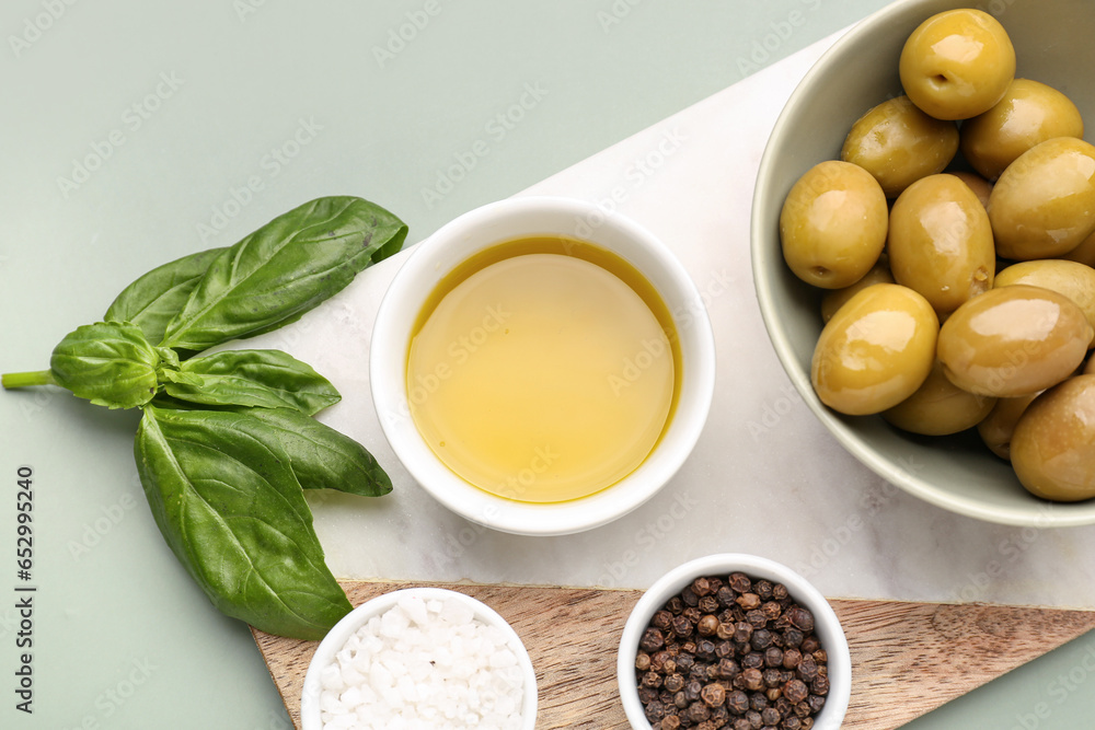 Bowls with ripe olives and oil on green background