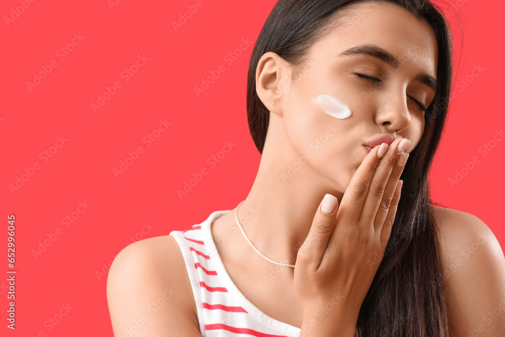 Young woman with sunscreen cream on her face blowing kiss against red background, closeup