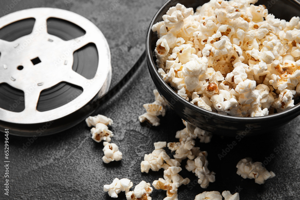 Bowl with tasty popcorn and film reel on black background