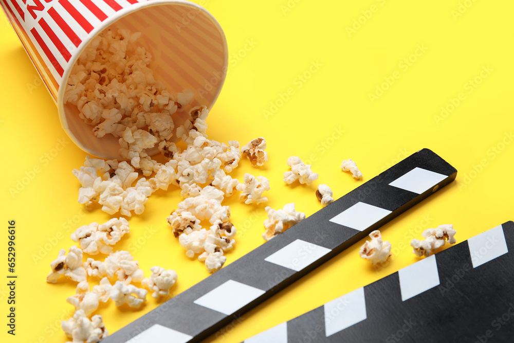 Bucket with tasty popcorn and clapperboard on yellow background