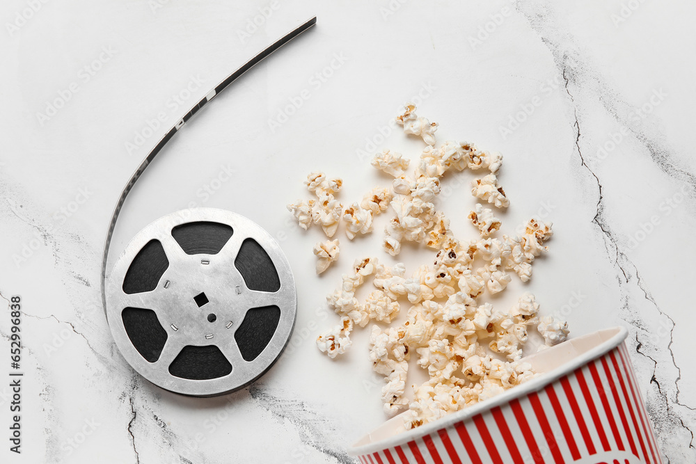 Bucket with tasty popcorn and film reel on white background