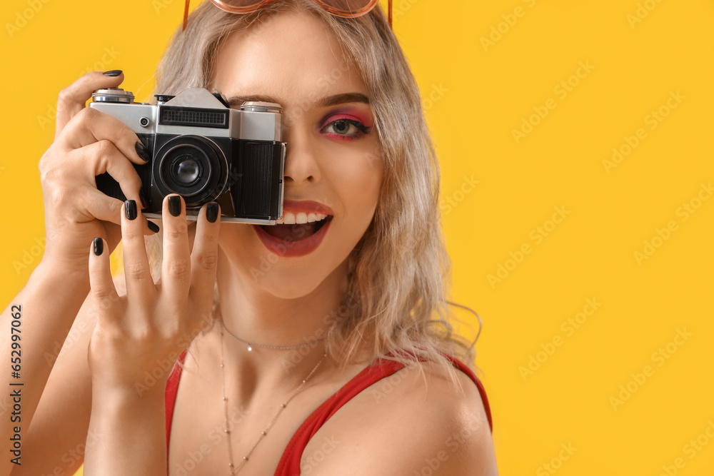 Young woman with photo camera on yellow background, closeup