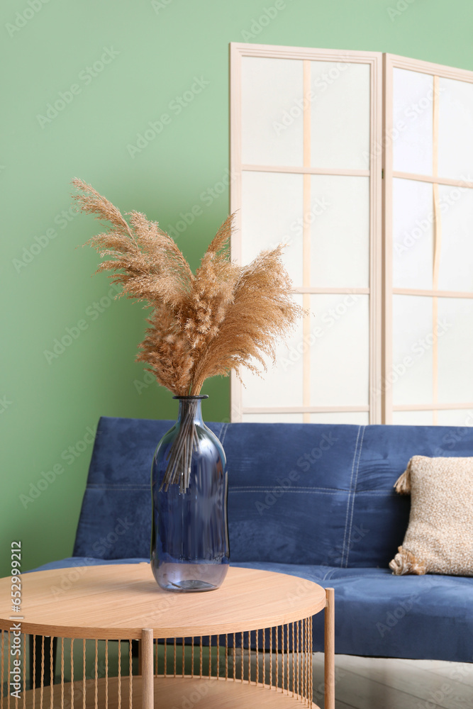 Wooden coffee table with dressing screen and couch near green wall