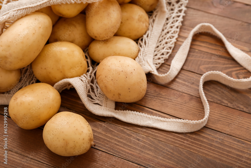 String bag with raw potatoes on wooden background