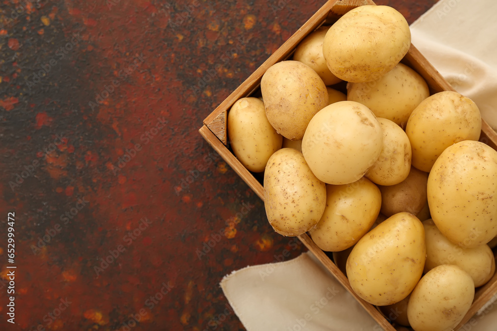 Wooden box with raw potatoes on dark background