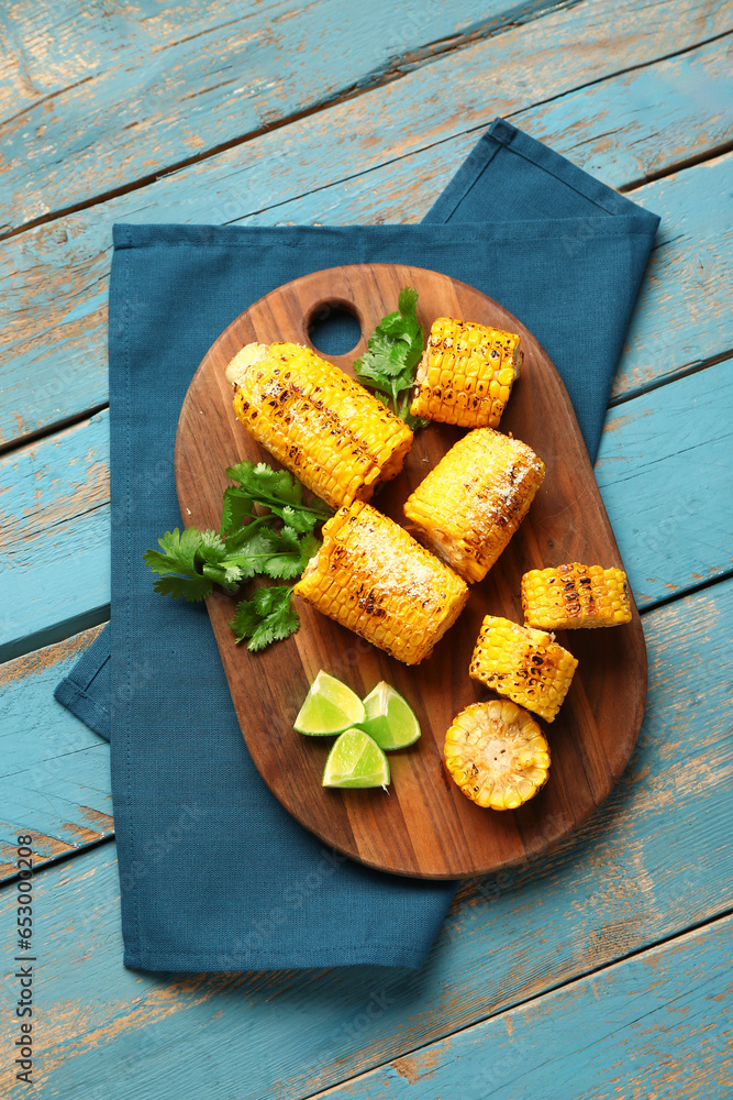 Board with cut tasty grilled corn cobs and parsley on blue wooden background