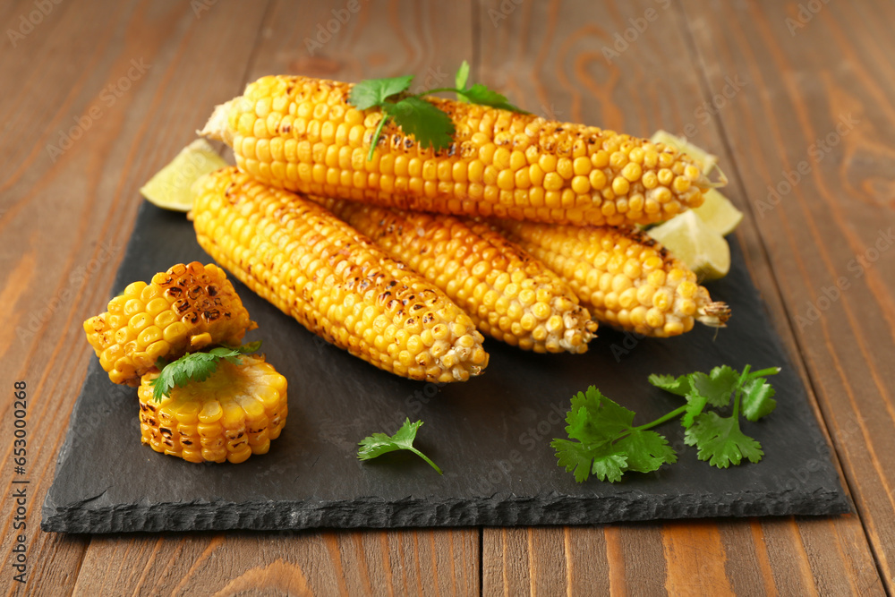 Board with tasty grilled corn cobs and lime on wooden background