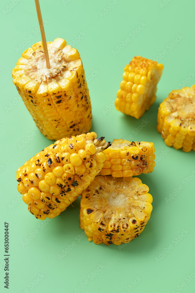 Cut tasty grilled corn cobs on green background