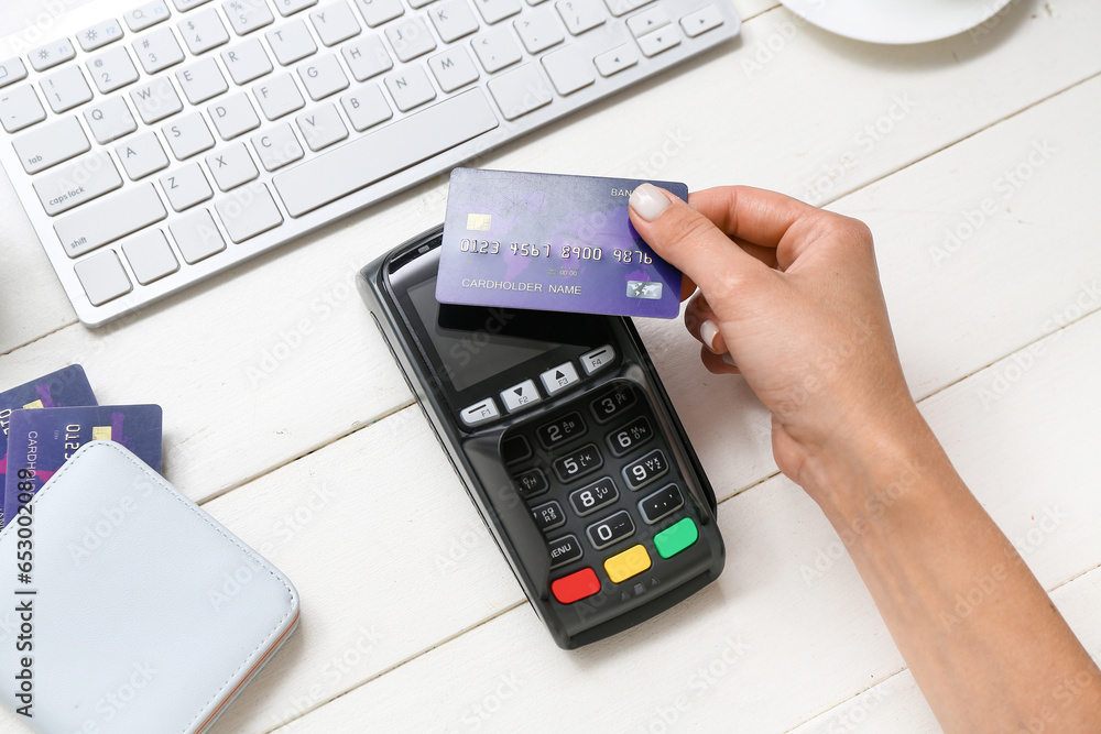 Female hand with payment terminal, keyboard and credit cards on white wooden background