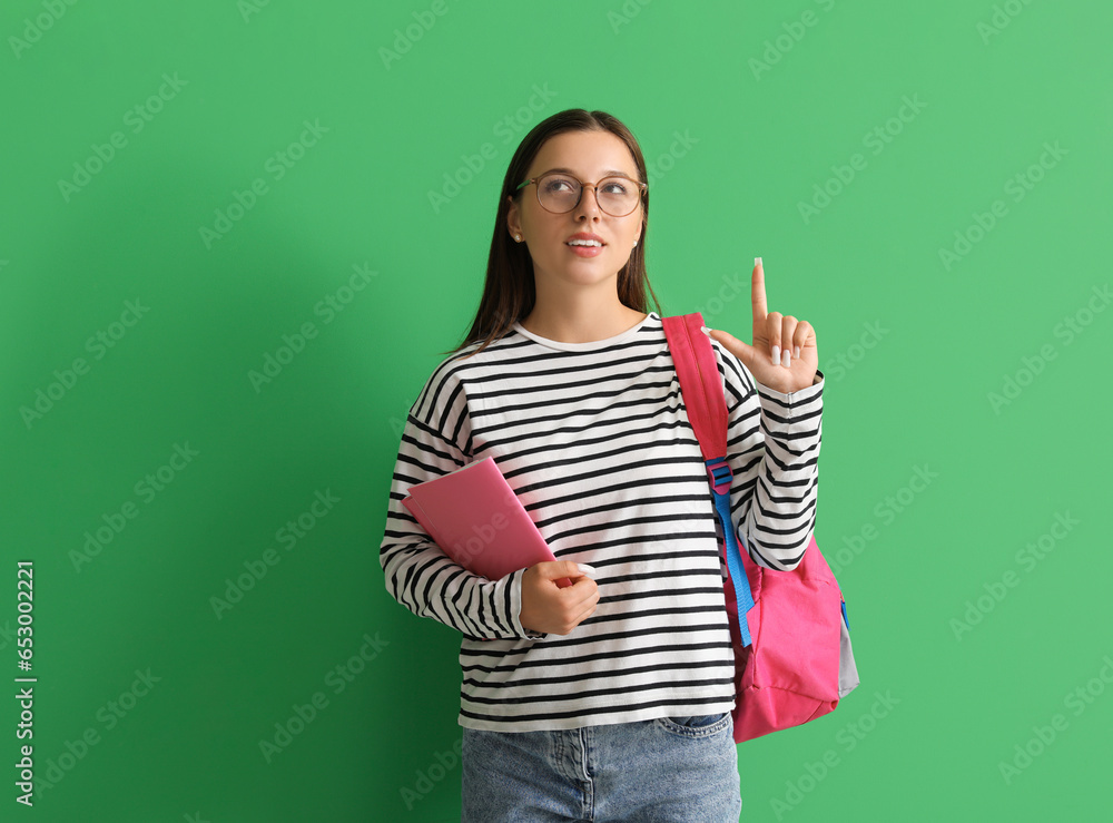 Happy female student with backpack and notebook pointing at something on green background