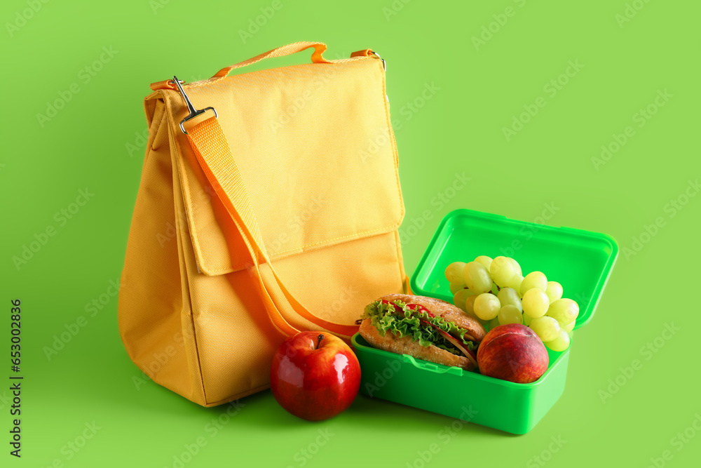 Bag and lunchbox with tasty food on green background