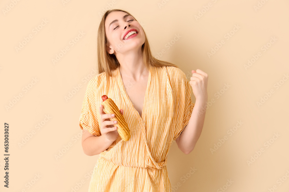 Happy young woman with tasty french hot dog on beige background