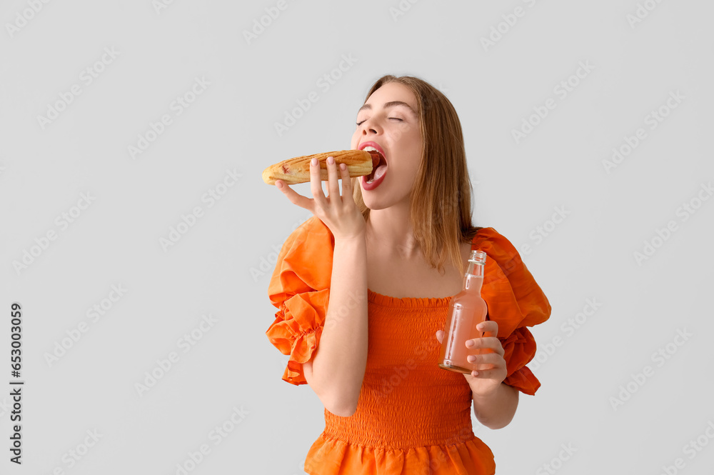 Pretty young woman with tasty hot dog and drink on grey background