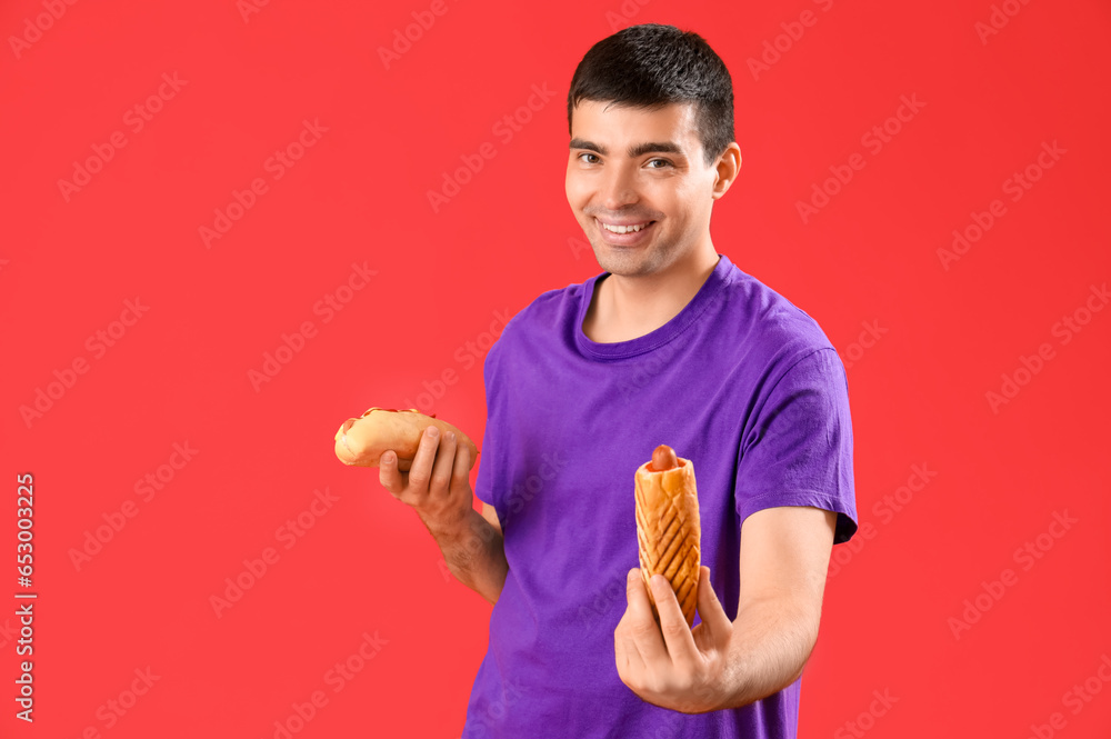 Happy young man with tasty hot dogs on red background