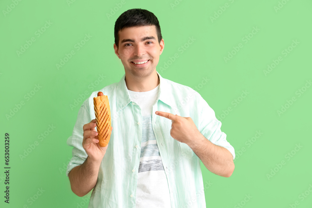 Happy young man with tasty french hot dog on green background