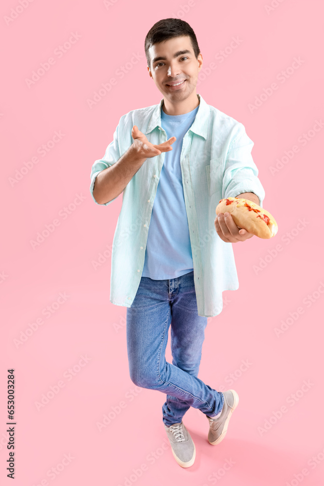 Handsome young man with tasty hot dog on pink background