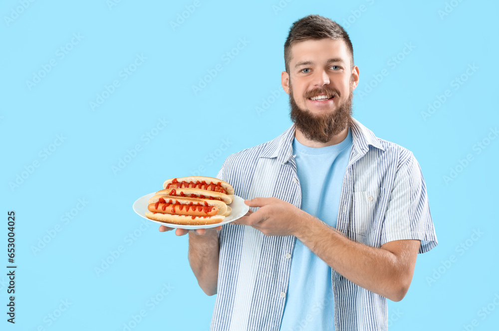 Portrait of happy young man with tasty hot dogs on plate against blue background