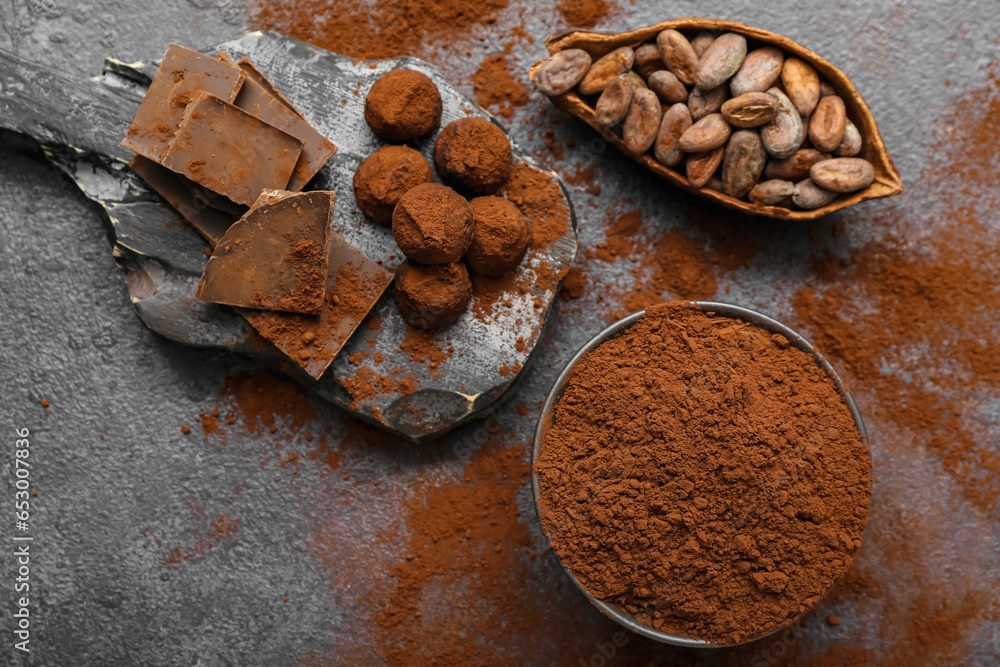 Bowl with cocoa powder, candies, beans and chocolate on black background