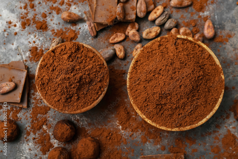 Bowls with cocoa powder, candies, beans and chocolate on black background