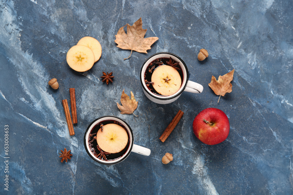 Cups of hot mulled wine with apple and cinnamon on blue background