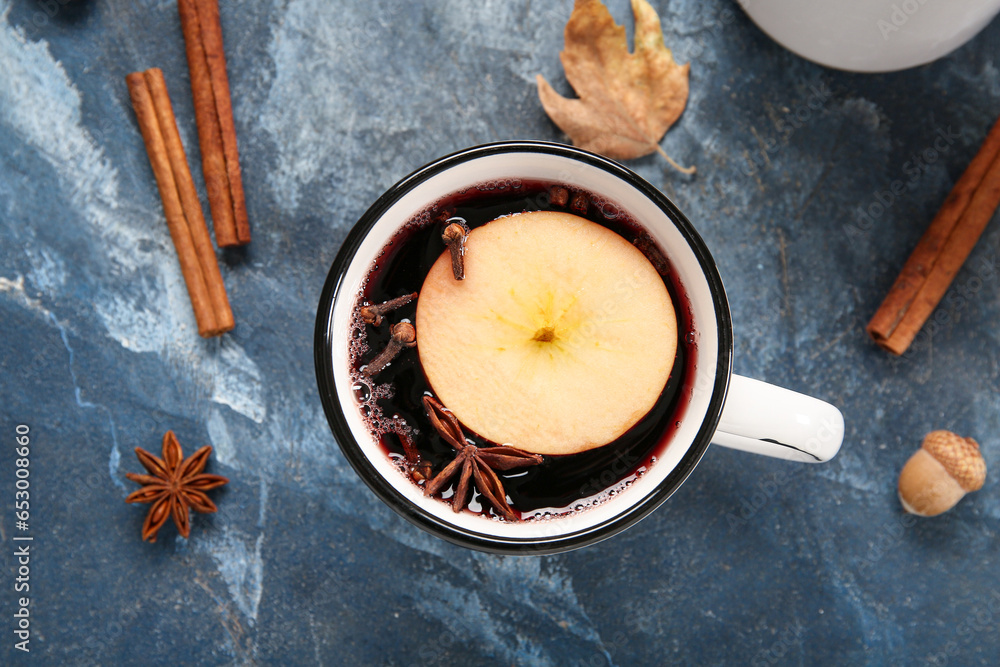 Cup of hot mulled wine with apple and cinnamon on blue background