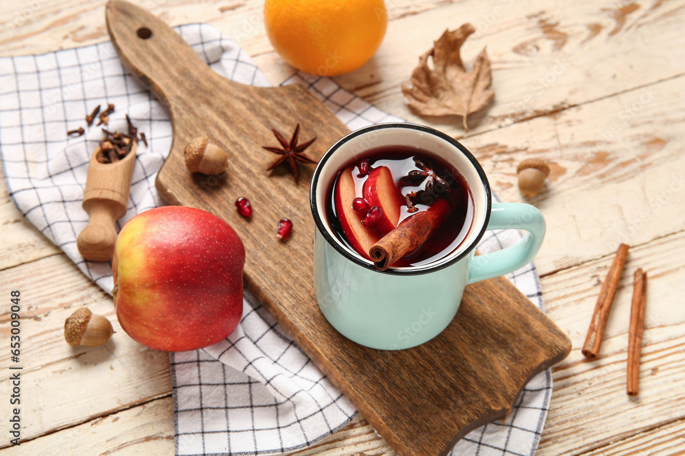 Cup of hot mulled wine with apple and pomegranate on white wooden background