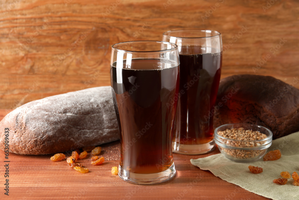 Glasses of tasty kvass, bread, raisins and wheat grains on wooden background