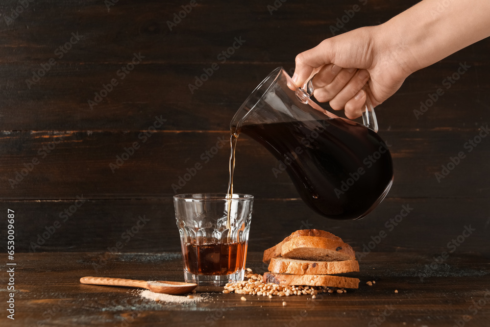 Woman pouring tasty kvass from jug into glass on wooden background