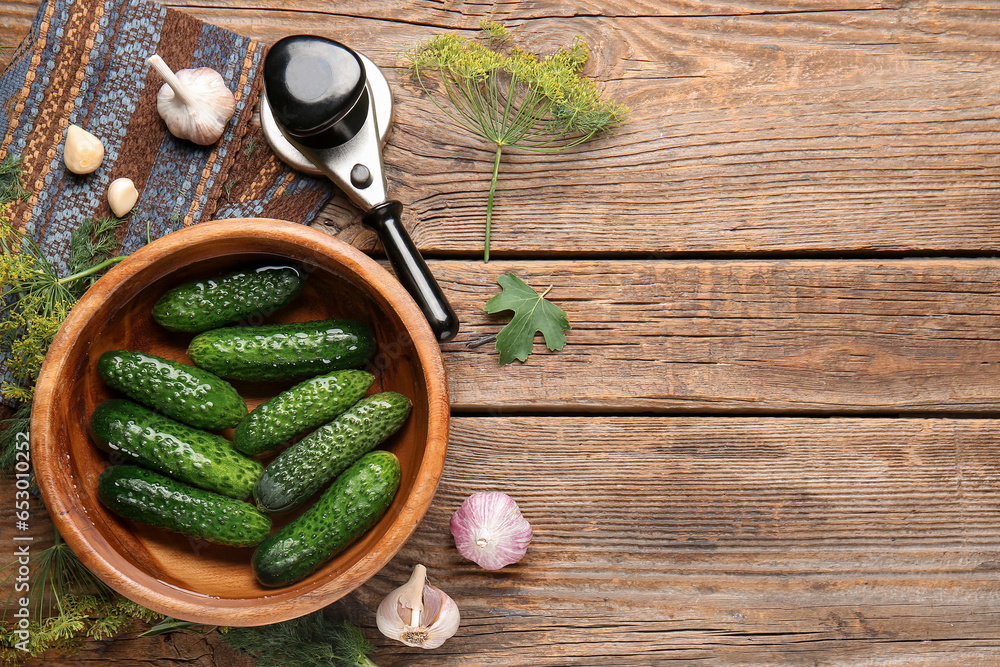 Bowl with fresh cucumbers and ingredients for canning on wooden background