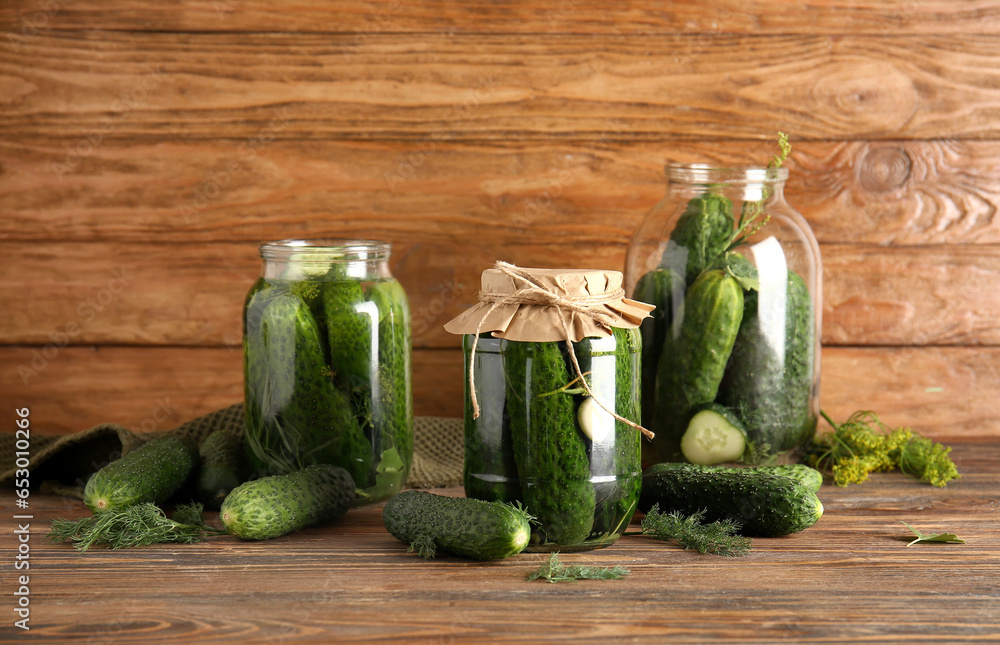 Jars with fresh and canned cucumbers on wooden background